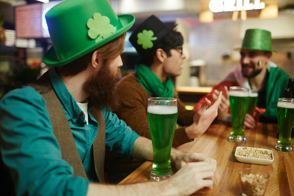Group of men in festive green hats enjoying green beer and conversation at a bar during a St. Patrick’s Day celebration